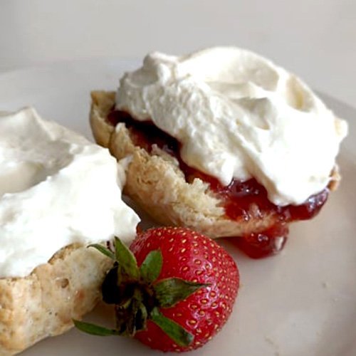 A scone cut open topped with strawberry jam and whipped fresh cream.