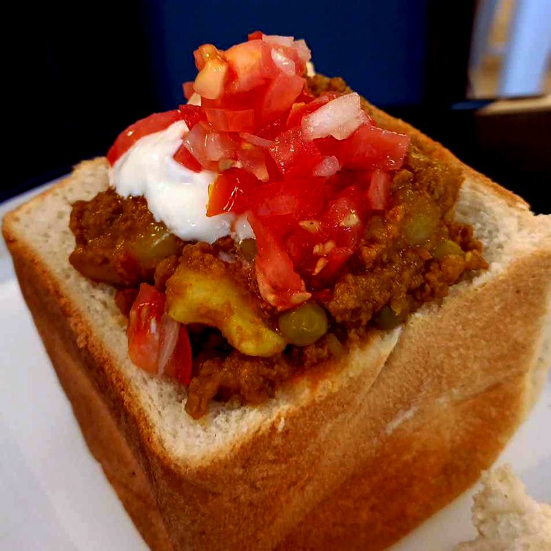 Hollowed out loaf of bread filled with curry topped with sambal and Greek yoghurt