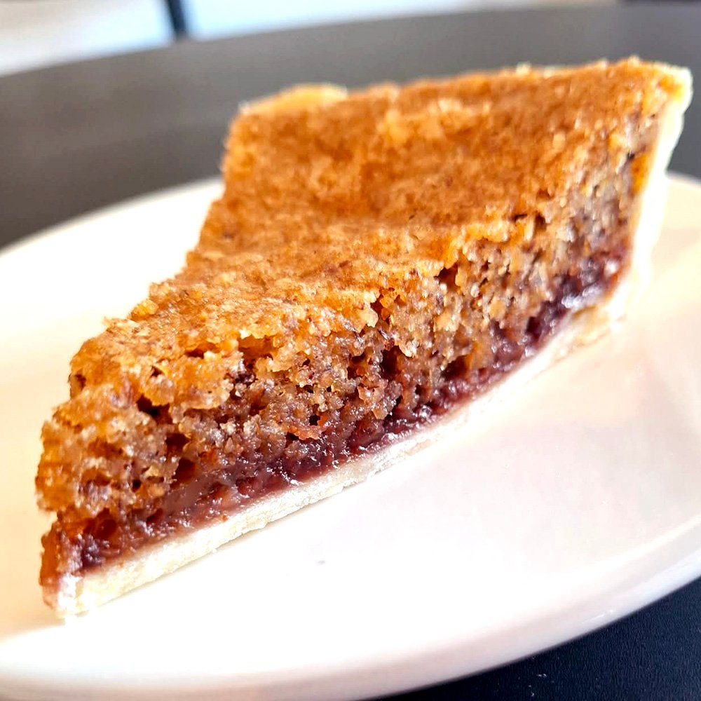 Slice of tart on a white saucer. Tart is almond meal over a jam base.