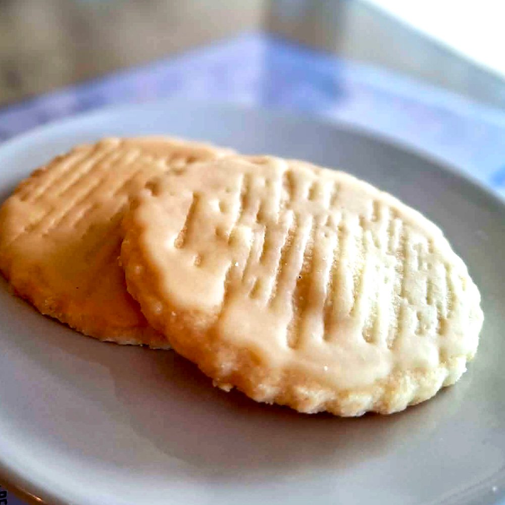 Two round shortbread biscuits with lemon drizzly on a white plate.