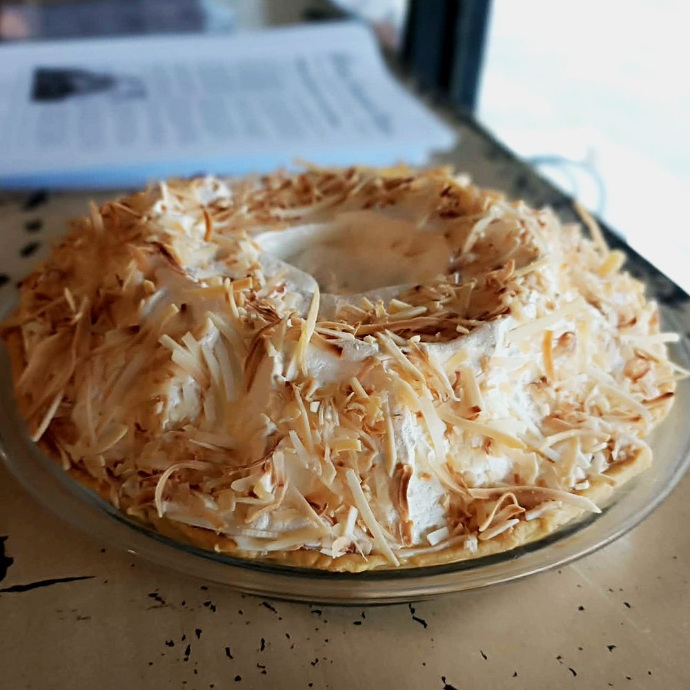 A whole coconut meringue tart, piled high with white meringue and toasted coconut.