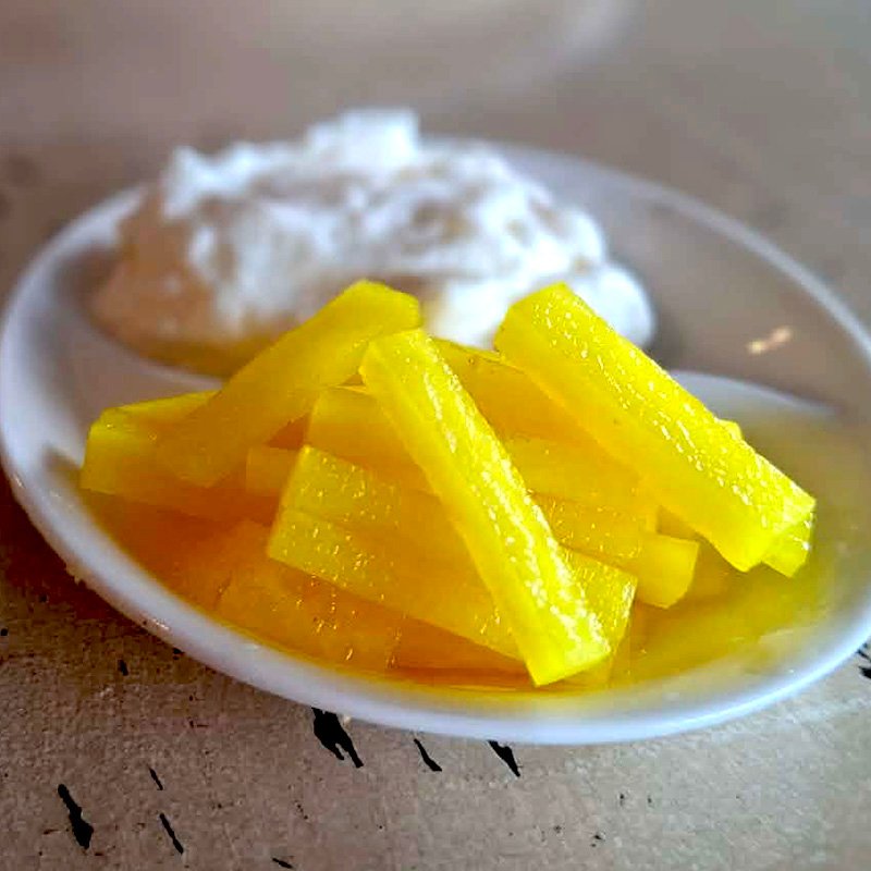 Two berth crucible containing a dollop of creamy labne and bright yellow batons of pickled daikon radish.