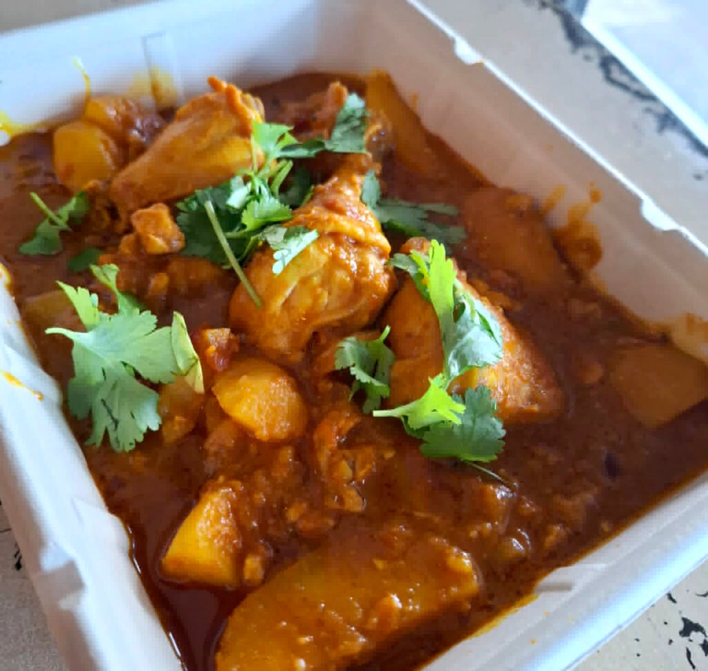 Close up of Cape Malay chicken curry showing bone in pieces of chicken and potatoes in sauce. Top sprinkled with coriander.