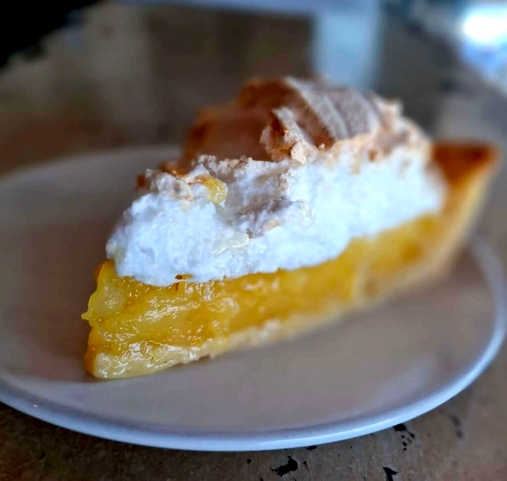 Wedge shaped slice of lime meringue tart on a white plate.